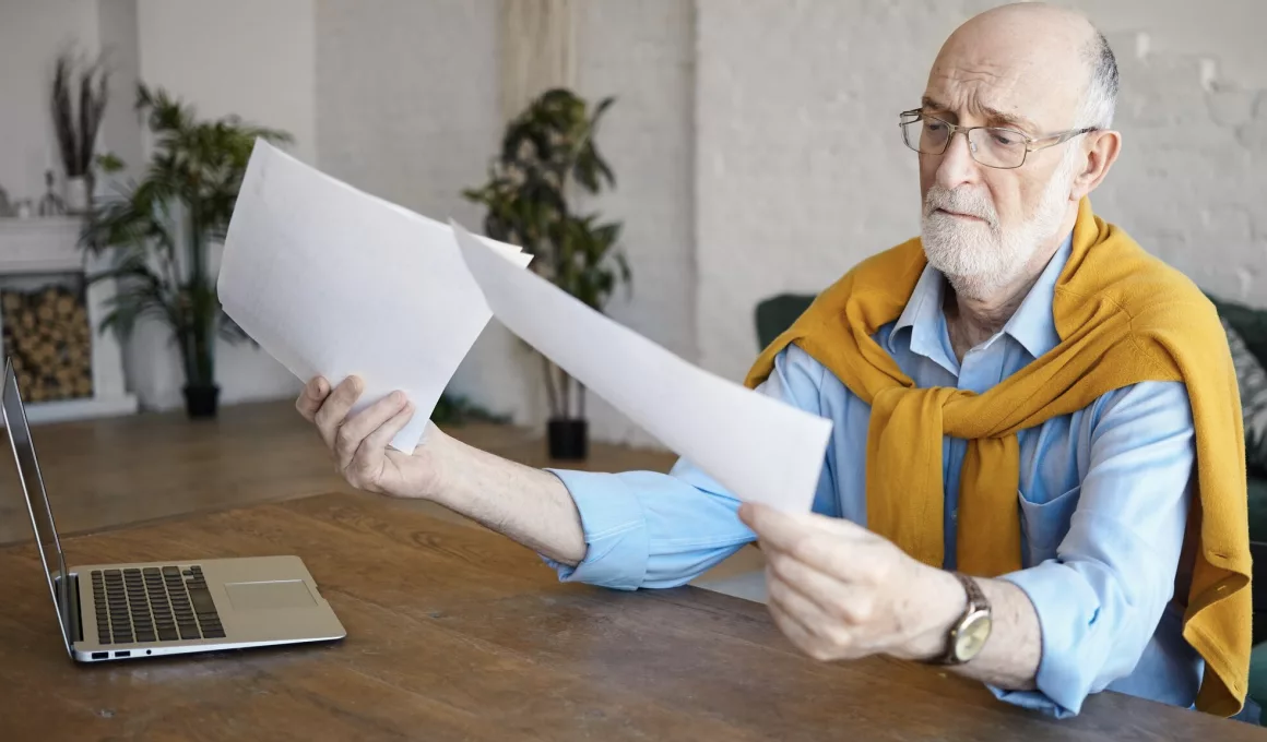 Homme âgé lisant des documents avec un ordinateur.