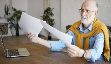 Homme âgé lisant des documents avec un ordinateur.