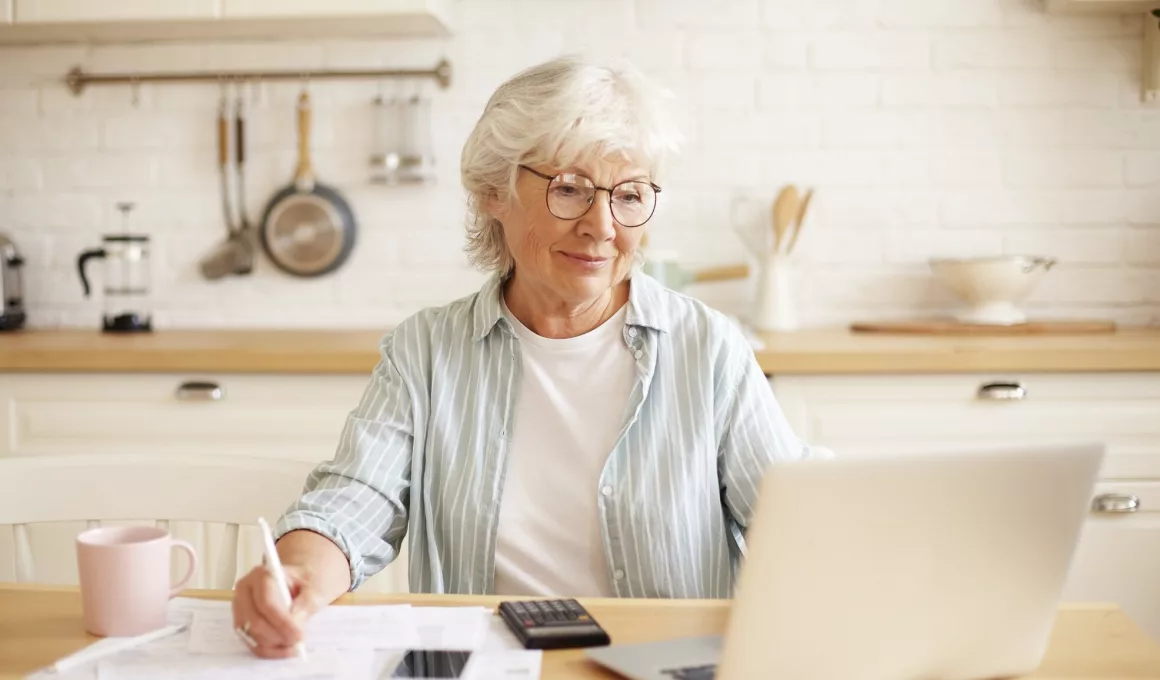 Femme senior travaillant sur ordinateur dans cuisine.