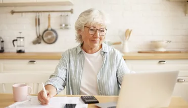 Femme senior travaillant sur ordinateur dans cuisine.