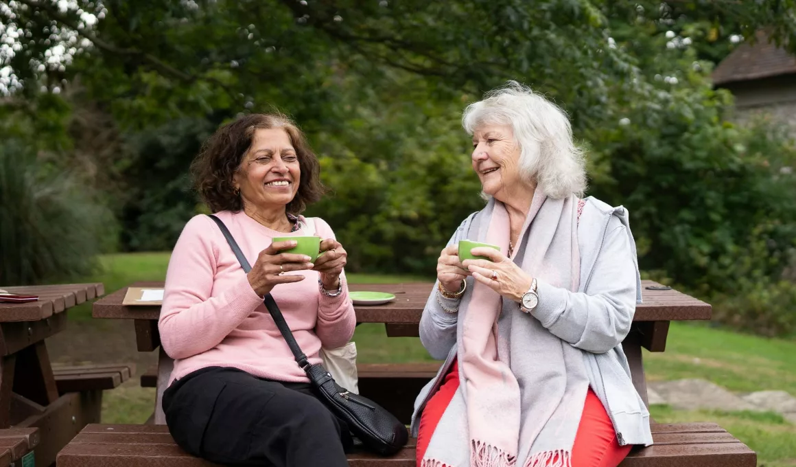 Deux femmes âgées souriantes buvant des boissons extérieures.