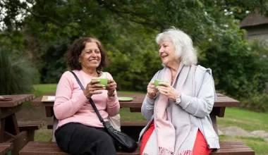 Deux femmes âgées souriantes buvant des boissons extérieures.